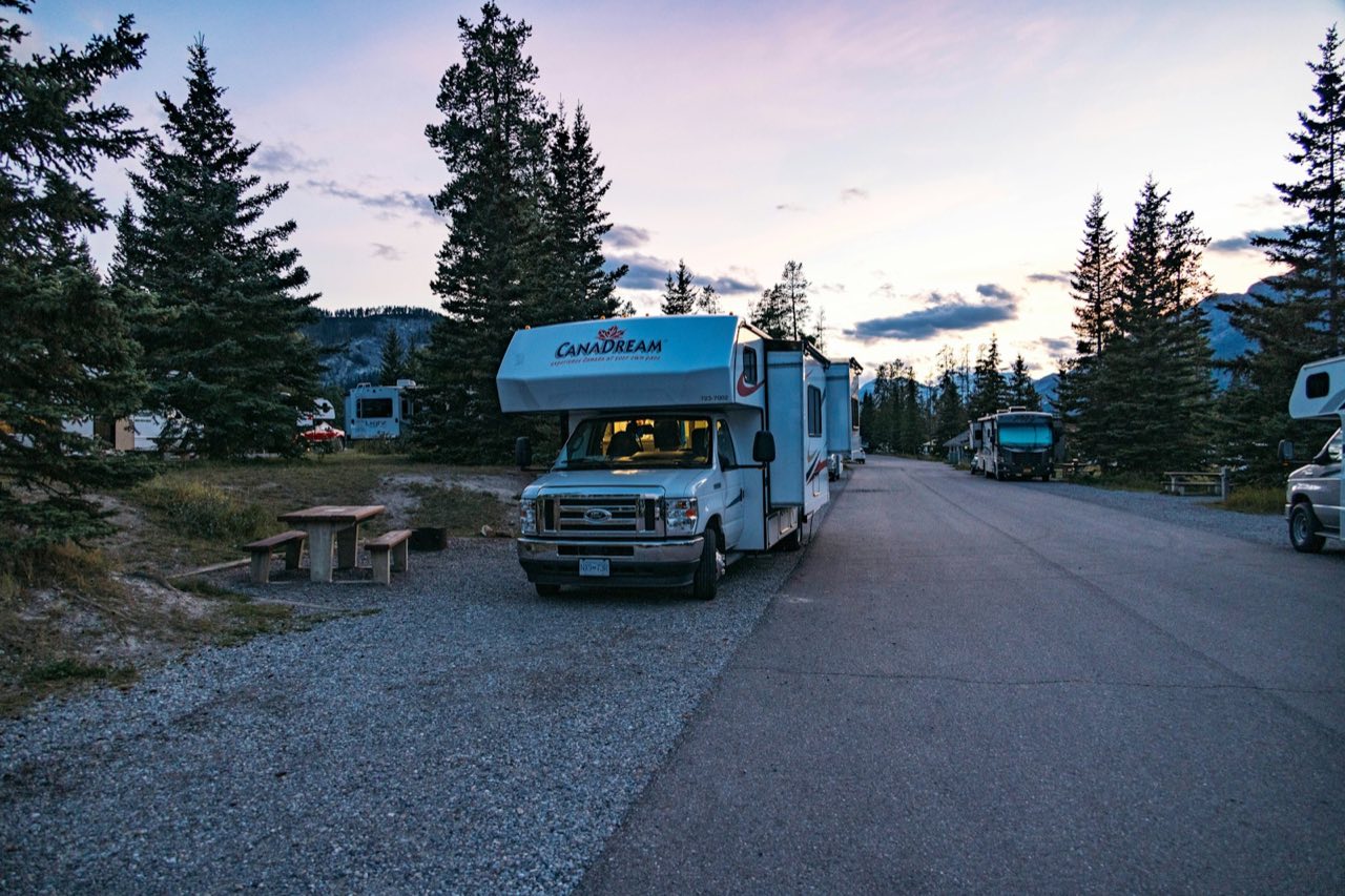 Motorhome parked for the night at a treed campground at dusk